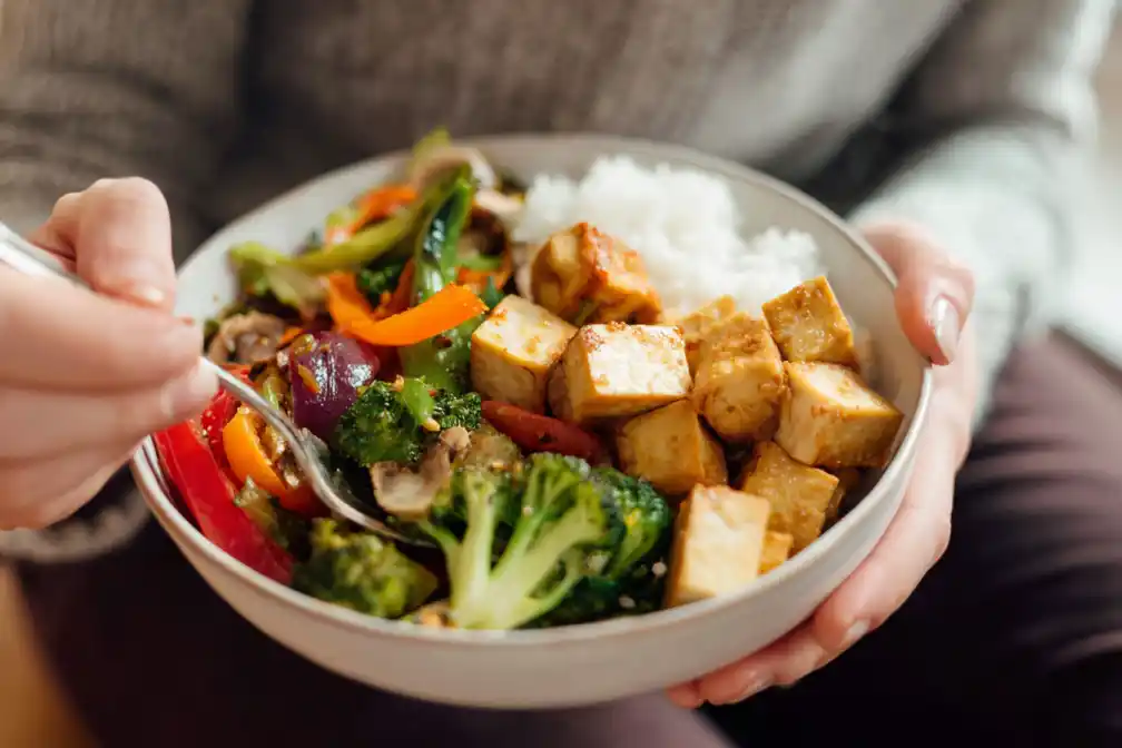 Hands placing vegetables and tofu on rice for gochujang bowl